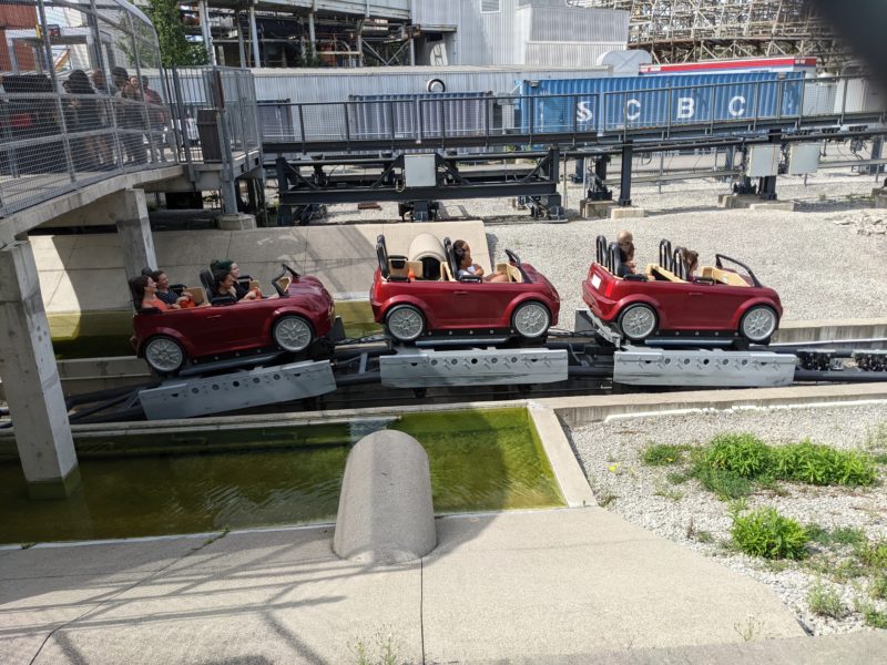 Car themed train on the Backlot Stunt Coaster going across the photo from left to right before going into the brake run of the ride.